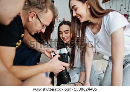 The team of photographers showing pictures on screen of camera for twins models girls on studio. Professional photographer on work.