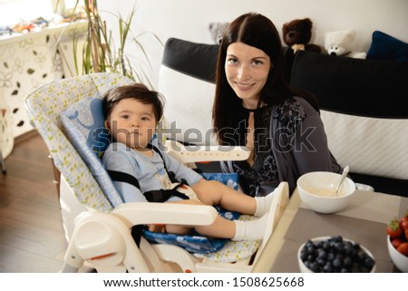 Mother feeding her baby son porridge in the child seat - Asian mixed ethnicity child Boy wearing blue body shirt with smiling bear cartoon Pregnant
