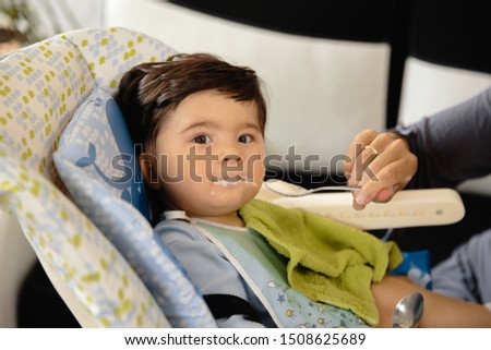 Mother feeding her baby son porridge in the child seat - Asian mixed ethnicity child Boy wearing blue body shirt with smiling bear cartoon Pregnant