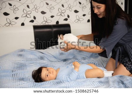 Pregnant Mother laying with her baby son on the bedroom bed playing and having fun - Asian mixed ethnicity child Boy wearing blue body shirt with smiling bear cartoon