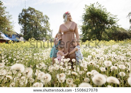 Mother having quality funny playing time with her baby girls at a park blowing dandelion - Young blonde hippie - Daughters wear similar dresses with strawberry print - Family values