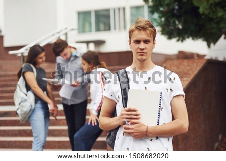 Guy posing for the camera. Group of young students in casual clothes near university at daytime.