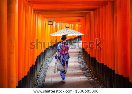 Woman in traditional kimono and umbrela walking at torii gates, Japan