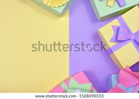 Flat lay background with pastel colored paper craft gift boxes framing copy space on right side lying on yellow and violet background