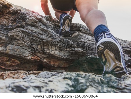 Middle aged woman climbing on the top of a cliff.Closeup legs and feets in sports shoes,  shooting from below. Royalty-Free Stock Photo #1508690864
