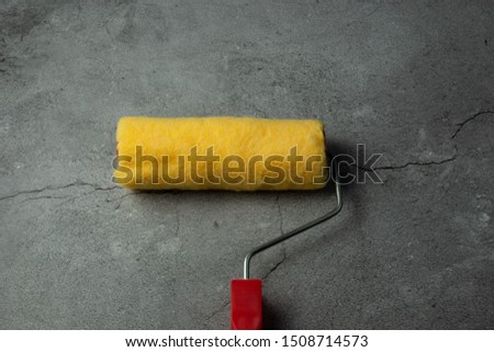 Red paint roller on concrete background.