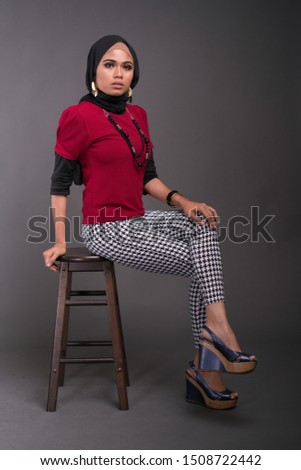 Attractive pretty hijab girl wearing a dark red shirt and retro pants isolated on grey background. Vintage fashion look concept.