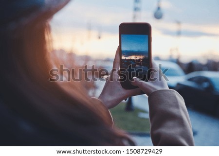 Girl hands holding phone and taking photo of a stunning sunset in big city
