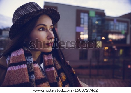 Close portrait of young smiling inspired female student dressed in casual warm autumn clothing standing in front of modern school or university after classes. Copy space
