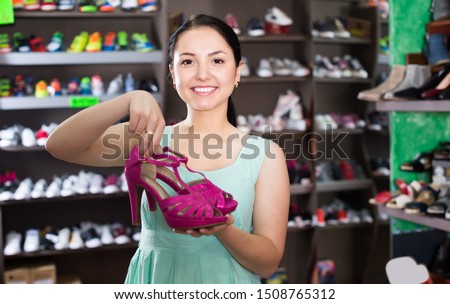 Charming woman customer is showing modern heeled sandals that she bought in shoes shop