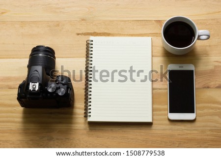 The photographer's top view, a wooden table with a camera, notebook, coffee, and smartphone.