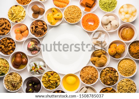 Rangoli of sweets and Farsan/snacks in bowls for Diwali with diya over white background