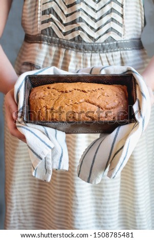 Young woman's hands holding a freshly baked loaf of homemade pumpkin bread baked in a vintage bread pan. Selective focus on sweet bread with blurred background. 