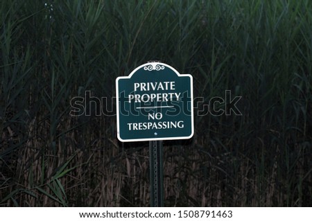Green and White sigh that reads "Private Property  No Trespassing".  It is placed in a field of reeds. 