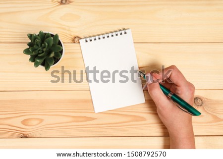 Modern workspace with smartphone, paper, notebook and female hands on wooden background. Top view. 