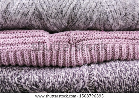 Bunch of knitted warm pastel color sweaters with different knitting patterns folded in stack, clearly visible texture. Stylish fall / winter season knitwear clothing. Close up, copy space for text.