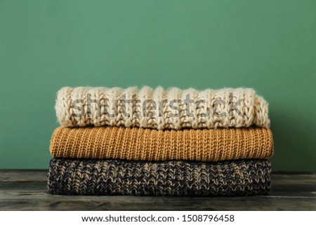 Bunch of knitted pastel color sweaters with different knitting patterns perfectly folded in stack on brown wooden table, green textured background. Fall winter season knitwear. Close up, copy space.