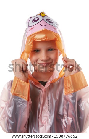 Medium close-up shot of a little girl dressed in a pink nacre raincoat buttoned with press-studs. The hood with child cartoon picture and wrists of the raincoat are fringed with orange elements. 