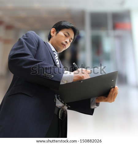 Businessman signing a document with modern office background