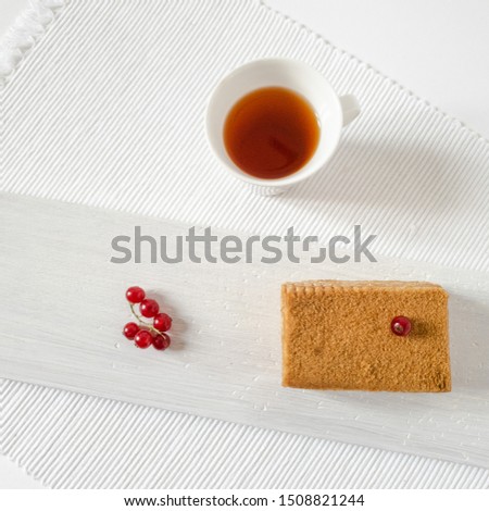Still life in a rustic style with pastries.  Slice of homemade cake, honey cake with red currant berries and a cup of tea on a wooden board and textured white napkin, top view.  Tasty snack