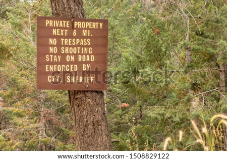 A brown wooden sign warns of private property, no trespassing, no shooting, stay on the road. 