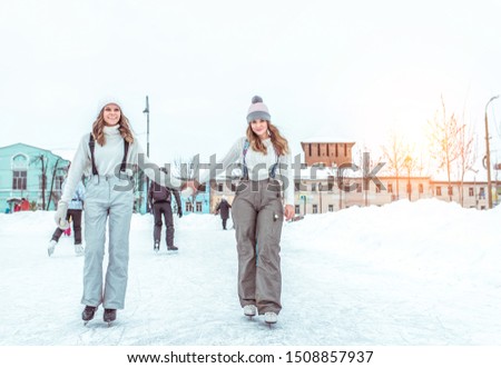 Two women girlfriends winter warm clothes, sweaters hats, happy smiling, relaxing weekends winter resort, ice skating, snowdrifts background, winter ice rink. Cheerful women. Free space for text