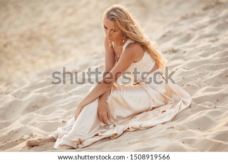 Portrait of beautiful bride is wearing fashion flying dress sitting on sand in the great desert in Dubai.