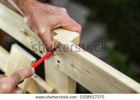 Adult carpenter craftsman with screwdriver screw the screw to fix the boards of a wooden fence. Housework do it yourself. 