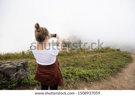 Back side of asian woman girl use smart mobile phone take photo of view of landscape mountain cover with fog in background,Travel concept.