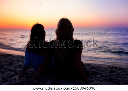 Rear View Of Two Young Women Looking At Sea At Sunset. Silhouettes of two young women watching at beach at colorful sunset