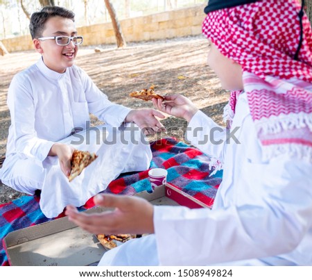 Happy arabic boys enjoying pizza together at the park