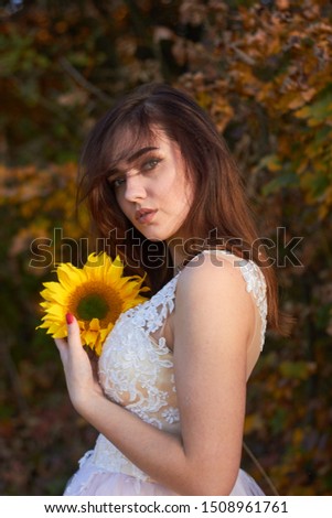 Beautiful lovely girl in a white dress with a sunflower in her hands. Sunlight plays on the field. Enjoy the nature. Autumn time.