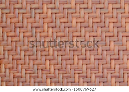 Smooth texture of wicker wood orange color. Symmetrical background weave of bamboo and straw. The texture of woven plant bark for furniture, close-up.
