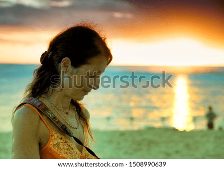 Woman at sunset on the beach looking at her camera pictures.