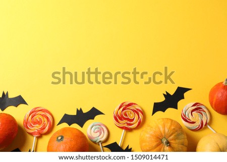 Candy, decorative bats and pumpkins on yellow background, top view