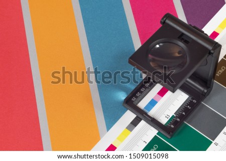 Black magnifying  glass standing on  the test print with colored background. Print loupe on offset printed sheet with basic colors control bars. Royalty-Free Stock Photo #1509015098