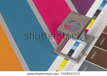 Silver magnifying glass standing on  the test print, colored background. Print loupe on offset printed sheet with basic colors control bars. Royalty-Free Stock Photo #1509015113