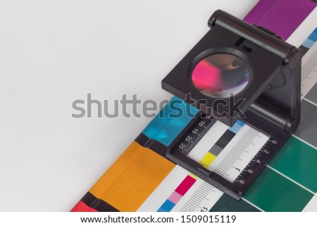 Black magnifying  glass standing on  the test print with colored background. Print loupe on offset printed sheet with basic colors control bars. Royalty-Free Stock Photo #1509015119