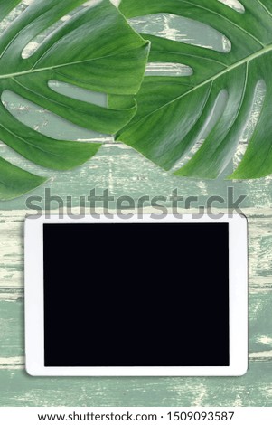 Monstera and tablet with a blank screen on a wooden old table. Copy space. 