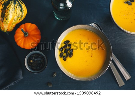 Pumpkin soup with cream and seeds in ceramic bowls on grunge black background. Top view