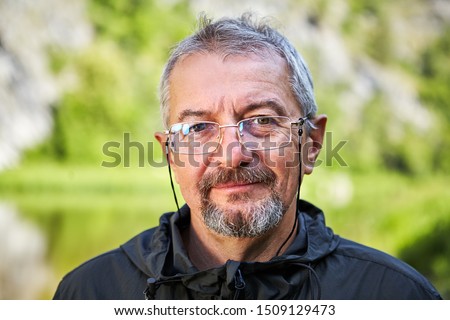 Close up portrait of an elderly intelligent man in glasses and with a gray beard. Smiling face of an educated man of retirement age. Outdoor portrait of an old man with a blurry green background. Royalty-Free Stock Photo #1509129473