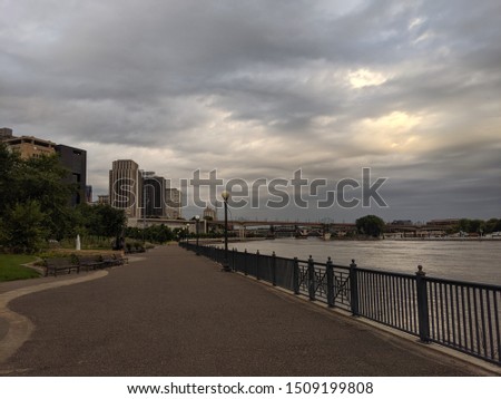 Urban park scene walking path with buildings in background along the Mississippi River with dramatic cloudy sky. Downtown St Paul , Minnesota , USA