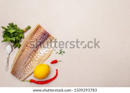 Raw cod loin fillet with lemon, sea salt, chili and cayenne pepper, parsley. Freshly thawed fish, healthy vegetarian food concept. Stone concrete background copy space top view