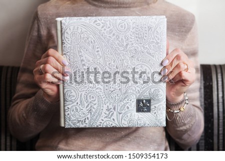 Woman holding a family photobook. White photo album in female hands. Wedding or family photoalbum with cover of genuine leather. White color with decorative stamping. 