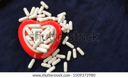 White capsule pills and hypodermic syringe are in heart shaped bowl isolated dark.
