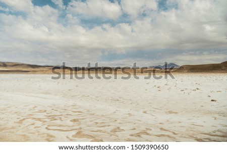 Dry, barren landscape with beautiful mountain background. Mountain range view, shot in Salt Flats of Uyuni, Bolivia.  Copy space, blue sky and sand dust foreground