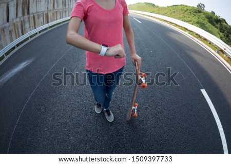 Skateboarder looking at her smartwatch on highway road