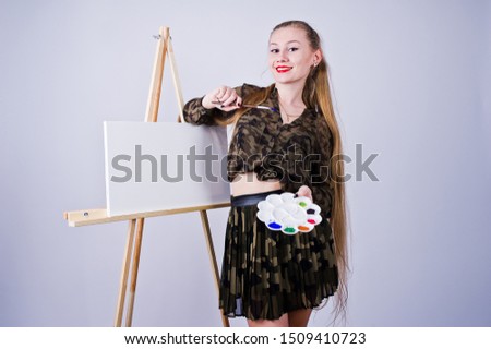 Beautiful woman artist painter with brushes and oil canvas posing in studio isolated on white.