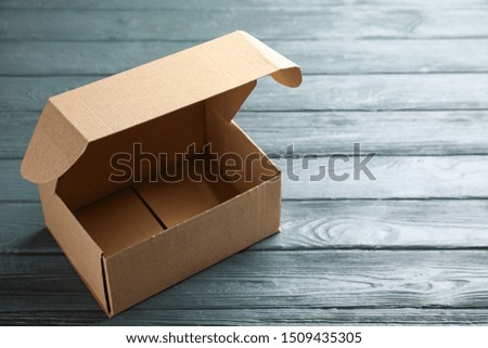 Open cardboard box on dark wooden table. Space for text