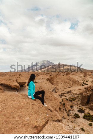 Hiker woman sitting & looking at Mountain range view, shot in Salt Flats of Uyuni, Bolivia.  Dry, barren landscape with beautiful mountain background. Tourist, hiking, climbing. Copy space, sand dust